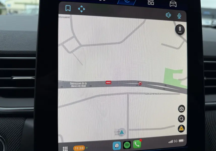 Gros plan sur les commandes à gauche du volant perforé du Renault Symbioz bleu iron, avec affichage numérique flou en arrière-plan.