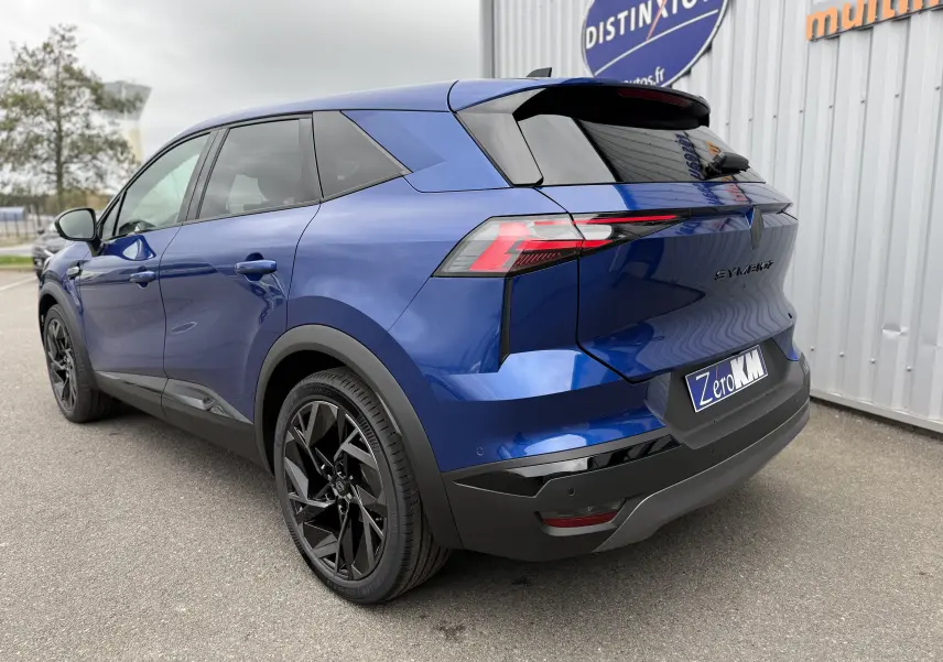 Renault Symbioz bleu Iron vu en 3/4 arrière droit, avec jantes noires et hayon électrique visible.