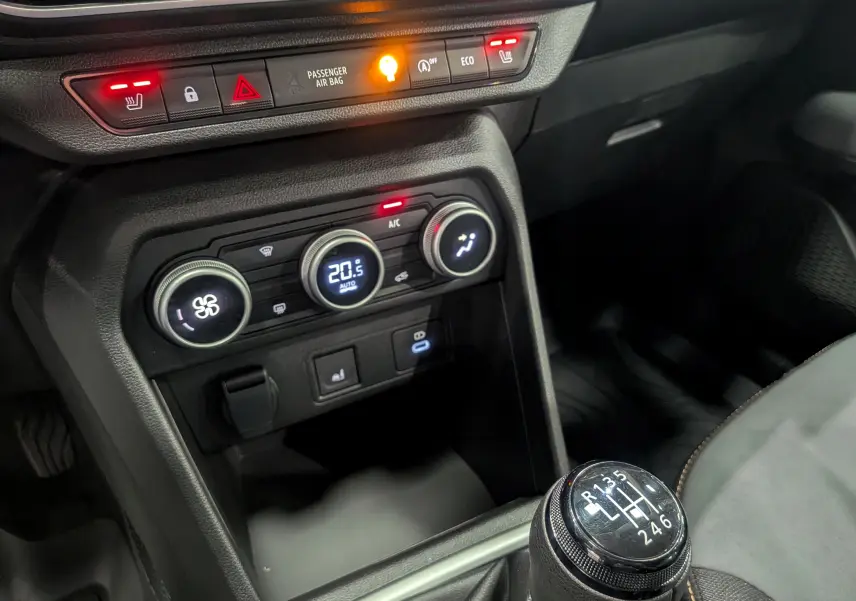 Gros plan sur la console centrale et levier de vitesses manuelle du Dacia Sandero Stepway gris, avec commandes climatisation et sièges chauffants allumés.