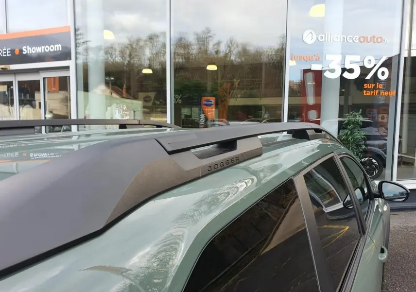 Vue rapprochée du toit côté droit du Dacia Jogger kaki métallisé avec barres de toit longitudinales et logo Jogger visible.