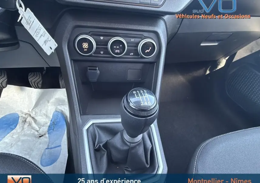 Gros plan sur le levier de vitesse manuel du Dacia Jogger gris, avec commandes de climatisation et console centrale visible.