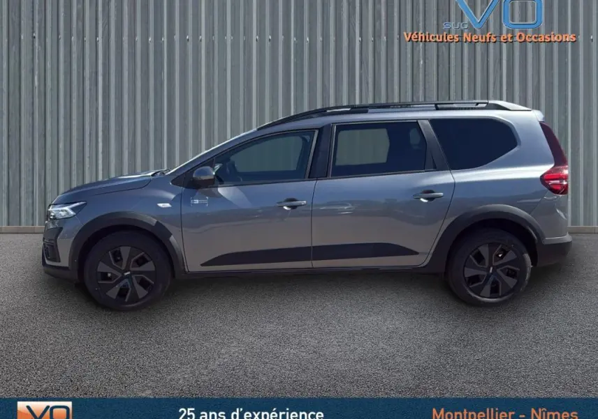Vue de profil côté gauche d'un Dacia Jogger gris 2025 avec barres de toit et jantes noires.