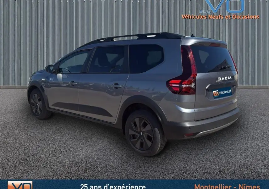 Vue 3/4 arrière droite d'un Dacia Jogger gris 2025 avec barres de toit et feux arrière LED distinctifs.