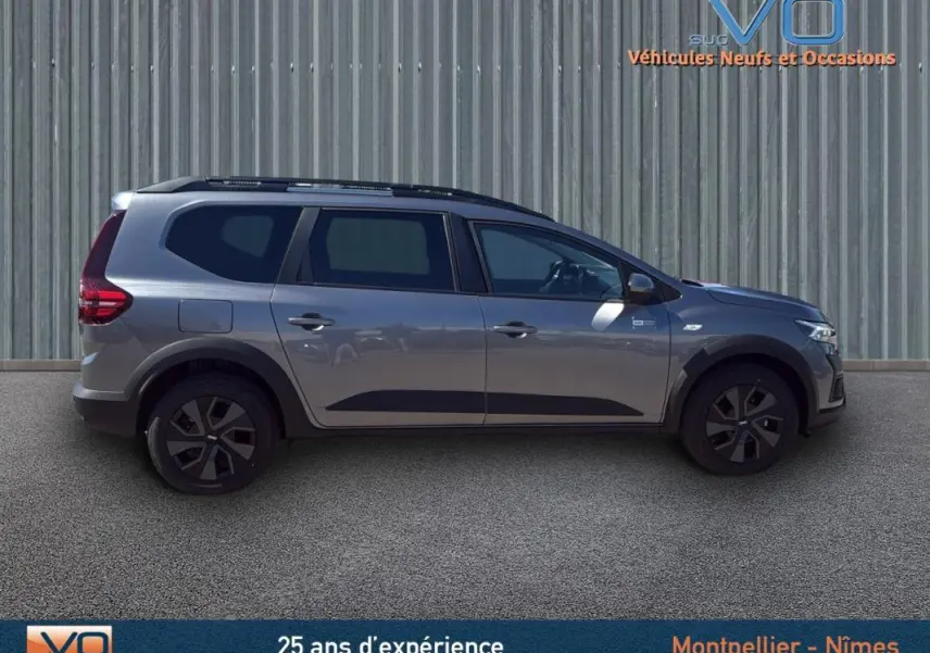 Profil côté droit du Dacia Jogger gris 2025 avec barres de toit et jantes noires, sur fond neutre extérieur.