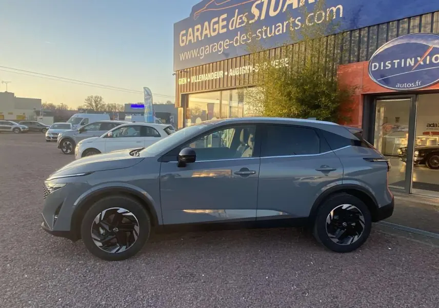 Vue de profil côté gauche d'un Nissan Qashqai gris ceramic garé devant un garage avec jantes noires au design moderne.