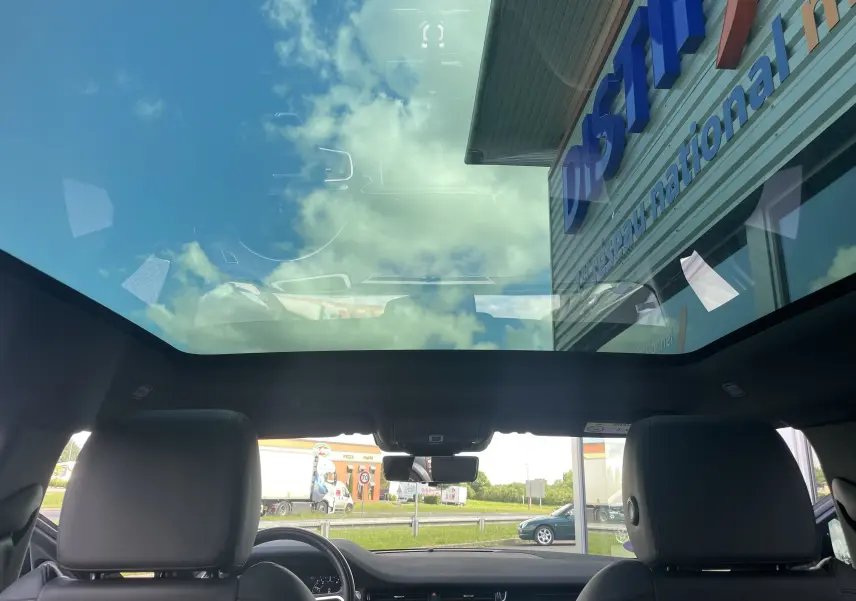 Vue intérieure du Range Rover Evoque bleu Portofino 2022, mettant en valeur son toit panoramique vitré et les sièges en cuir noir.