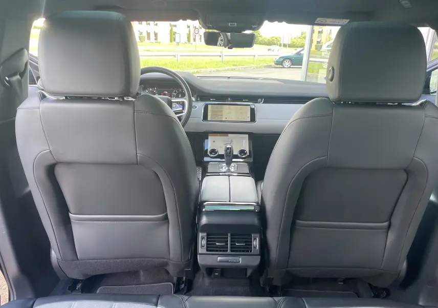 Vue intérieure arrière du Range Rover Evoque 2022, sièges en cuir gris noir et console centrale moderne avec écran tactile.