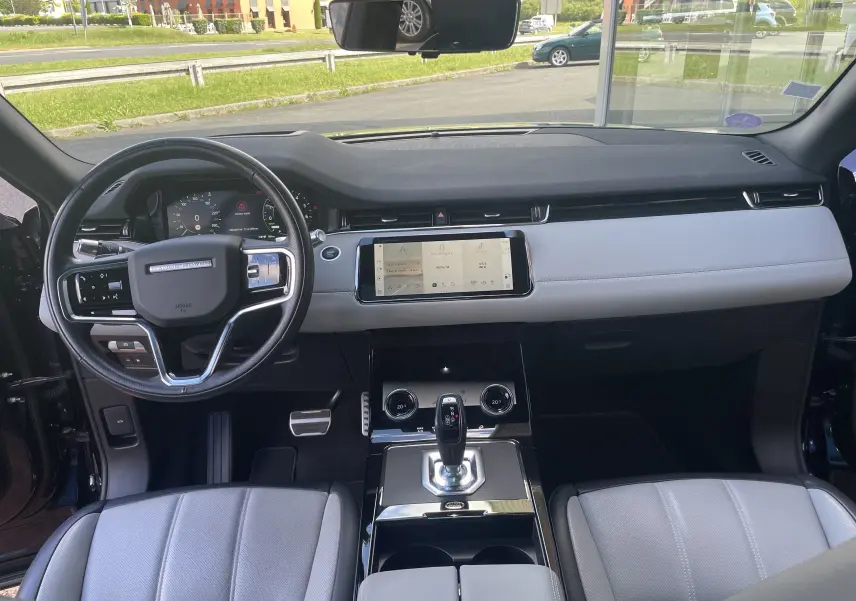 Vue intérieure avant du Range Rover Evoque 2022 avec tableau de bord gris clair, volant noir et écran tactile central.