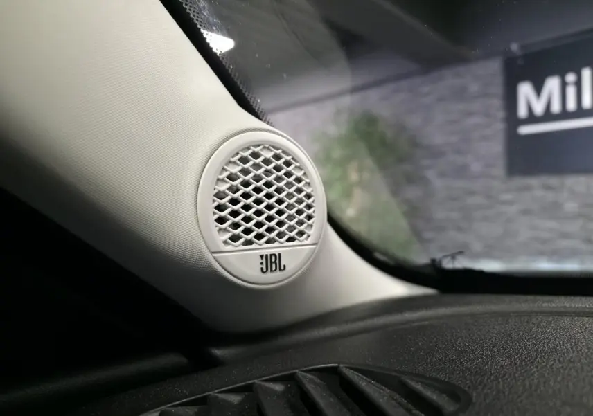 Gros plan sur l'enceinte JBL blanche intégrée à l'angle gauche du tableau de bord noir du Jeep Avenger gris.