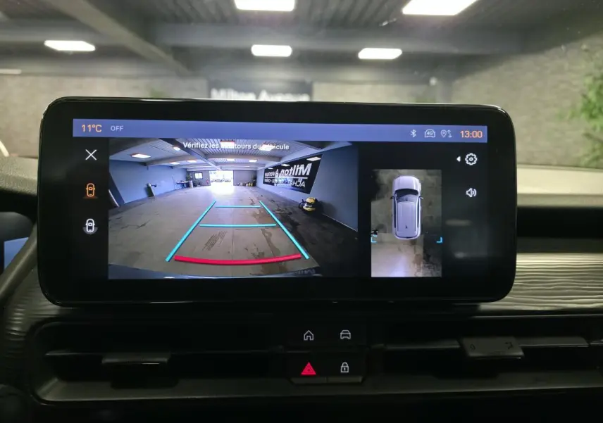 Écran tactile intérieur montrant la caméra de recul et vue aérienne du Jeep Avenger gris dans un garage.