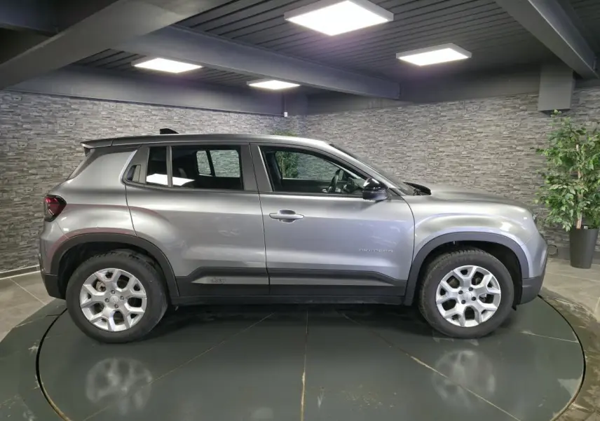 Vue de profil côté gauche d'un Jeep Avenger gris métallisé avec jantes alliage 17 pouces dans un showroom.