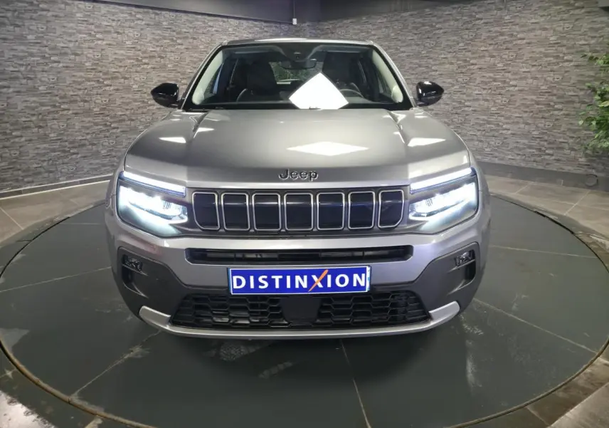 Vue frontale du Jeep Avenger gris avec phares LED allumés et calandre distinctive à sept fentes.