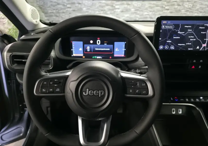 Vue intérieure centrée sur le volant Jeep noir avec tableau de bord numérique et écran tactile de navigation.