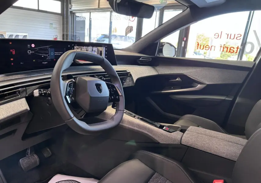 Vue intérieure côté conducteur du Peugeot 3008 hybride 2026, avec volant compact, tableau de bord numérique et habillage tissu gris.
