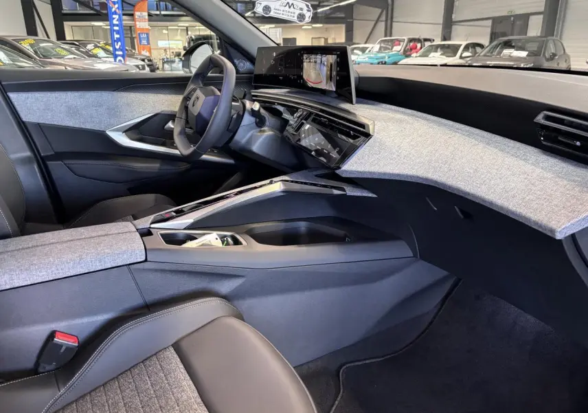 Vue intérieure côté conducteur du Peugeot 3008 Hybrid 2026, tableau de bord avec écran incurvé et décor tissu gris chiné.