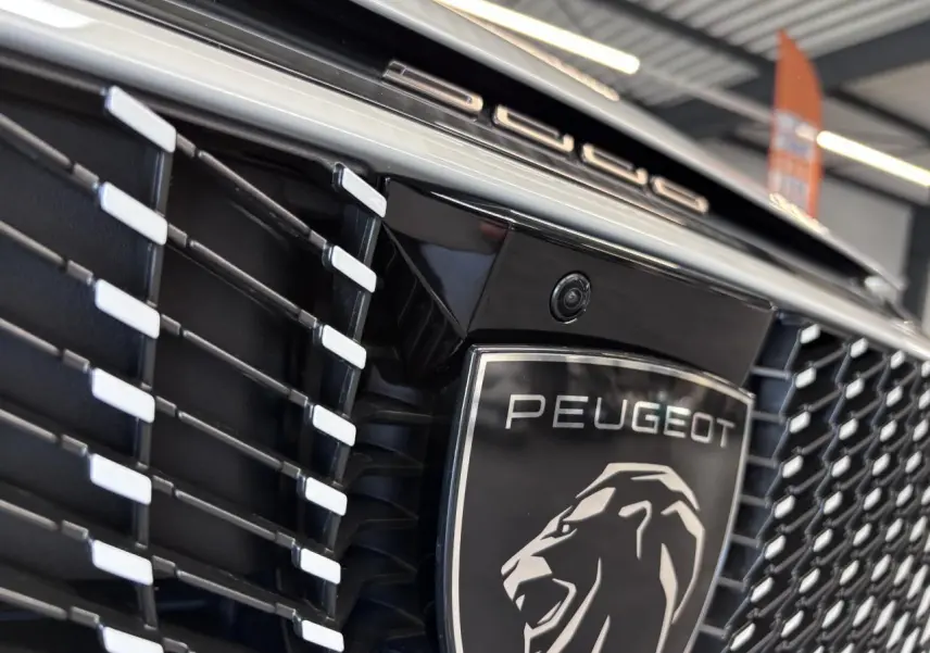 Gros plan sur la calandre noire laquée du Peugeot 3008 blanc avec logo lion et inscription Peugeot en chrome.
