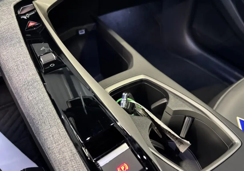 Gros plan sur la console centrale noire laquée et tissu gris chiné du Peugeot 3008 hybride avec frein de stationnement électrique activé.