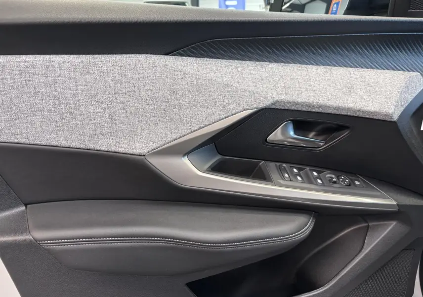 Gros plan sur la garniture intérieure de porte côté gauche du Peugeot 3008 blanc, avec tissu gris et commandes électriques.