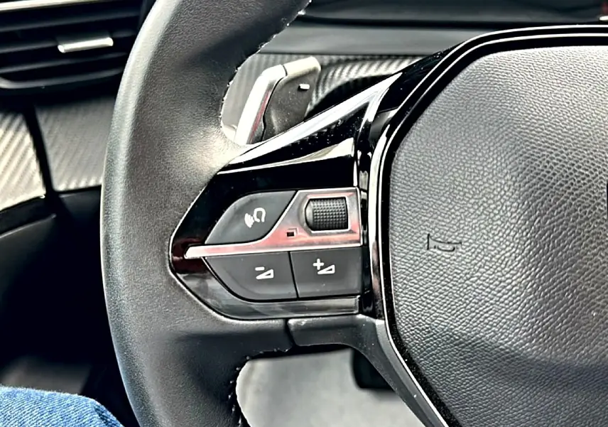 Gros plan sur le volant noir multifonction du Peugeot 2008 1.2 hybrid 145 style, avec commandes audio intégrées.