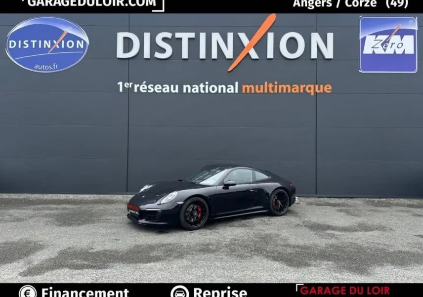 Vue 3/4 avant droite d'une Porsche 911 Carrera GTS Coupé noire avec jantes noires et étriers rouges, stationnée devant un mur gris.