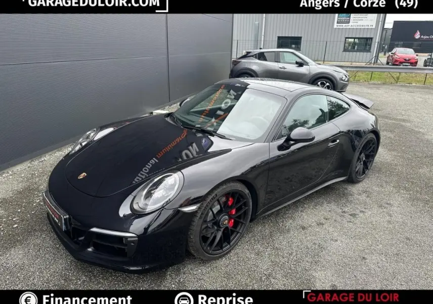 Vue 3/4 avant droite d'une Porsche 911 Carrera GTS Coupé noire avec jantes noires et étriers rouges, stationnée sur sol gravillonné.