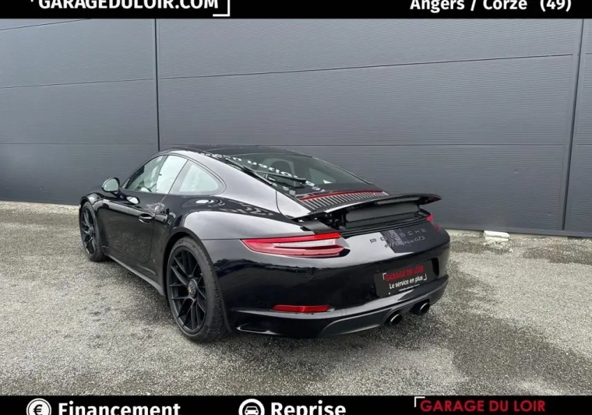 Vue 3/4 arrière droite d'une Porsche 911 Carrera GTS Coupé noire avec aileron arrière déployé sur sol gris.
