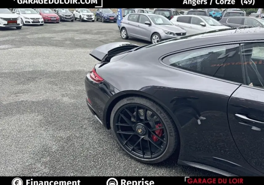 Vue 3/4 arrière droite d'une Porsche 911 Carrera GTS Coupé noire avec aileron arrière relevé et jantes noires.