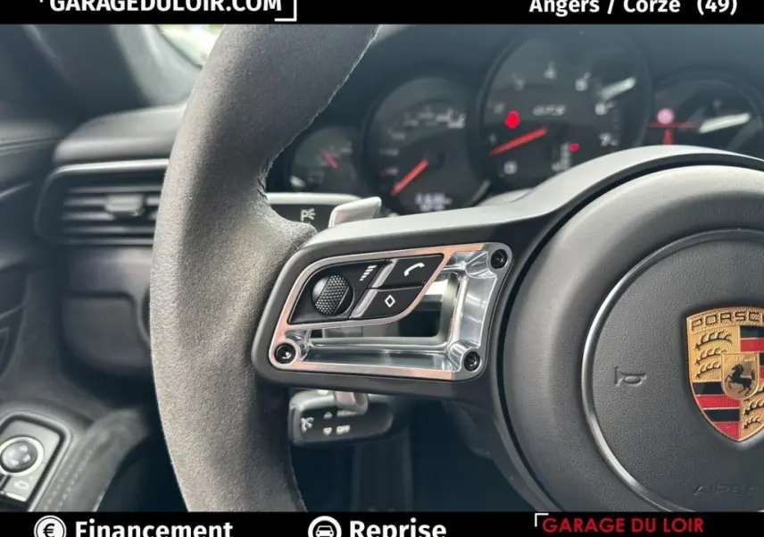 Gros plan sur le volant en alcantara côté gauche avec commandes intégrées et logo Porsche visible au centre.