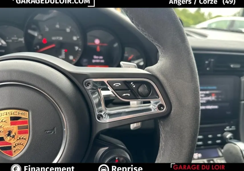 Gros plan sur le volant en alcantara côté droit avec commandes et logo Porsche visible, intérieur noir de la 911 Carrera GTS.