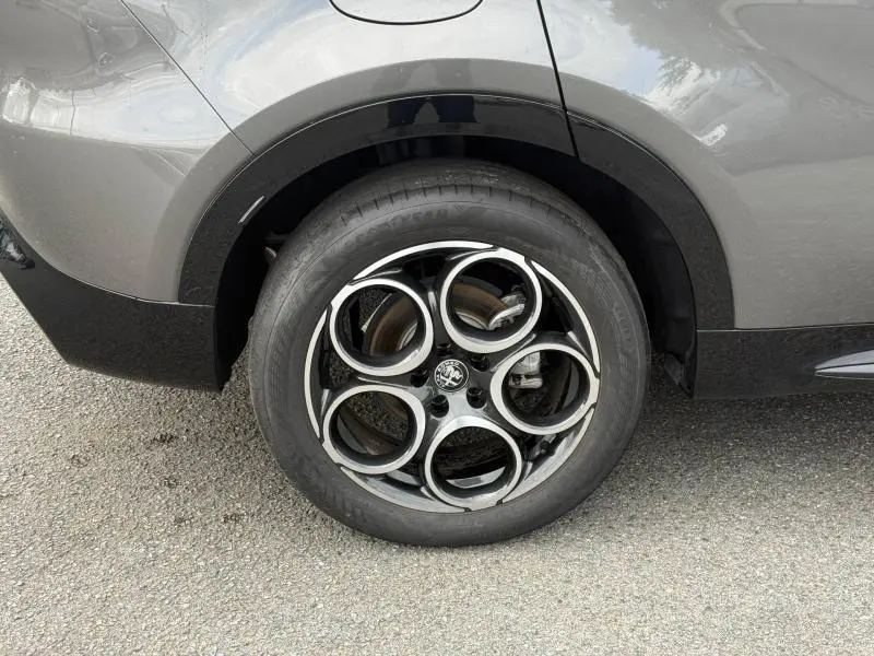 Gros plan sur la roue arrière droite de l'Alfa Romeo Tonale gris Vesuvio métallisé avec jante alu à cinq cercles entrelacés.