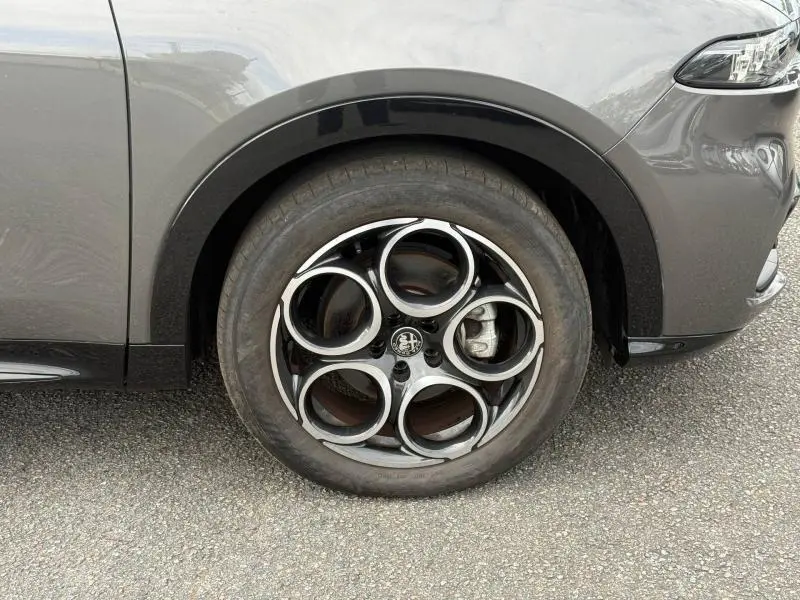 Gros plan sur la roue avant gauche de l'Alfa Romeo Tonale gris Vesuvio métallisé avec jante alu à cinq cercles distinctifs.
