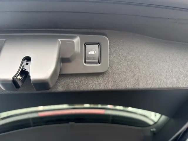 Gros plan sur le bouton de hayon motorisé noir, situé sur le bord intérieur du coffre du Renault Austral bleu.