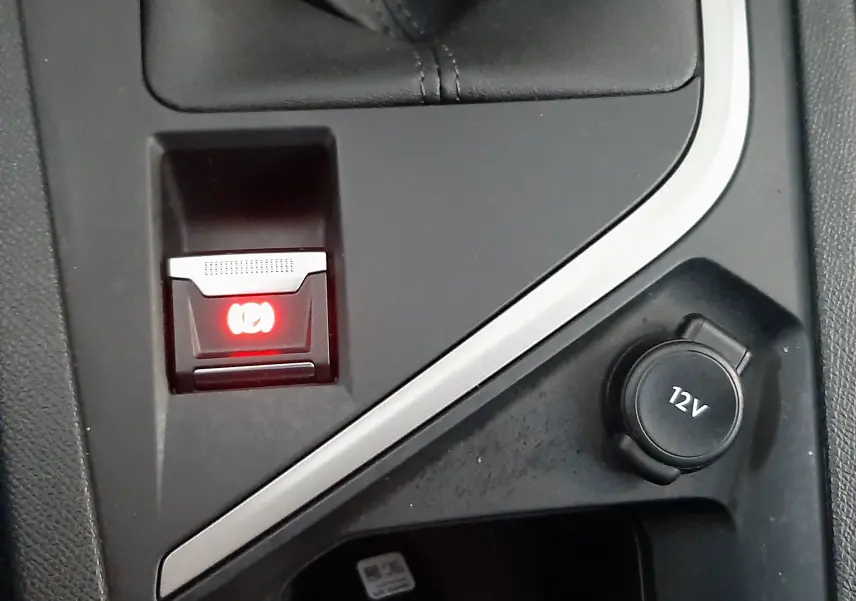 Gros plan sur la console centrale de la Peugeot 308 blanche, montrant le frein à main électronique et prise 12V.