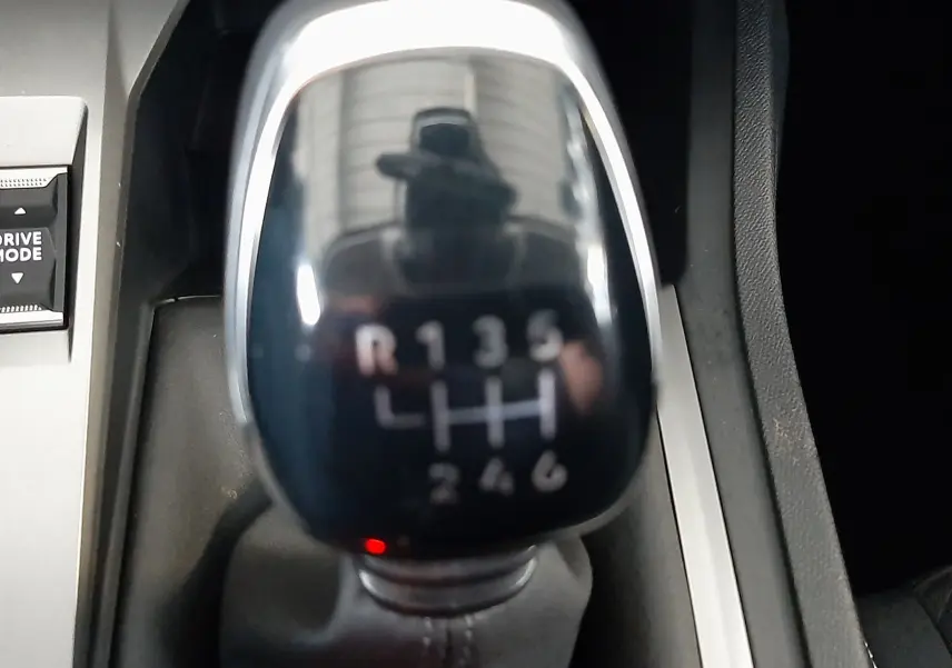 Gros plan sur le levier de vitesses manuel noir brillant de la Peugeot 308 blanche, montrant les six rapports et la marche arrière.
