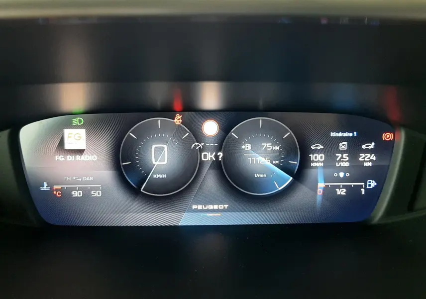 Tableau de bord numérique de Peugeot 308 blanc banquise, affichant vitesse, compte-tours et informations de trajet.