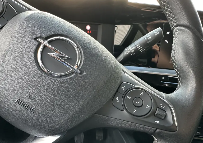 Gros plan sur le volant en cuir noir de l'Opel Mokka Elegance 2021 avec commandes intégrées et logo Opel central.