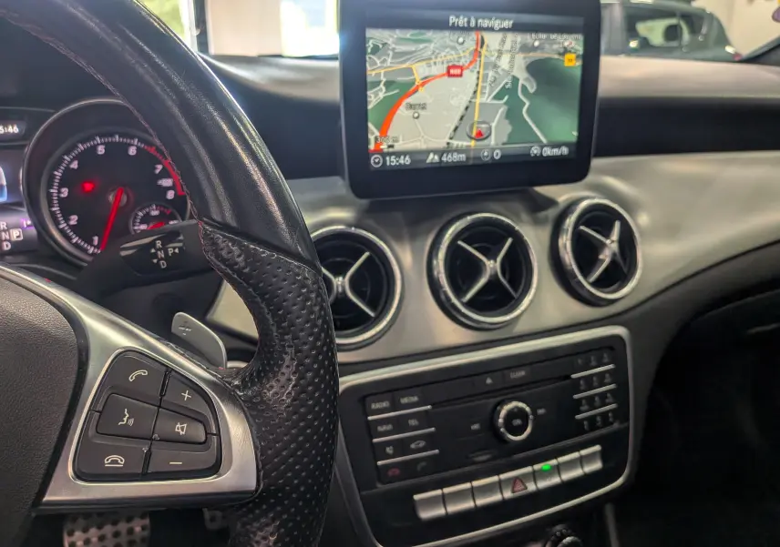 Vue intérieure de la Mercedes CLA 200 2017 montrant le volant, les commandes et l'écran de navigation central.