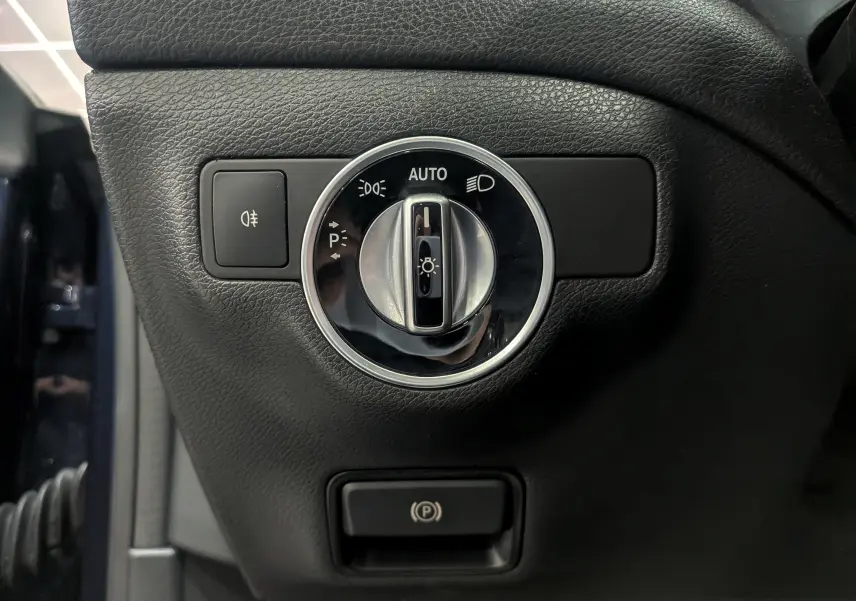 Gros plan sur le bouton de commande des phares et frein à main électrique dans une Mercedes Classe CLA 200 bleu Cavansite de 2017.