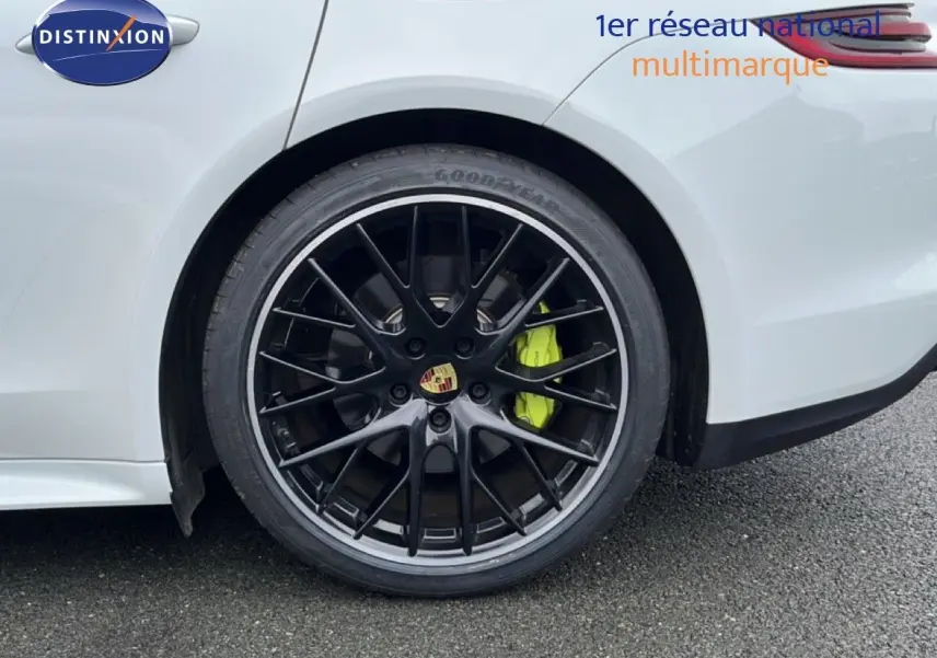 Gros plan sur la roue arrière droite noire brillante avec étrier de frein vert fluo d'une Porsche Panamera 4 E-Hybrid blanche.