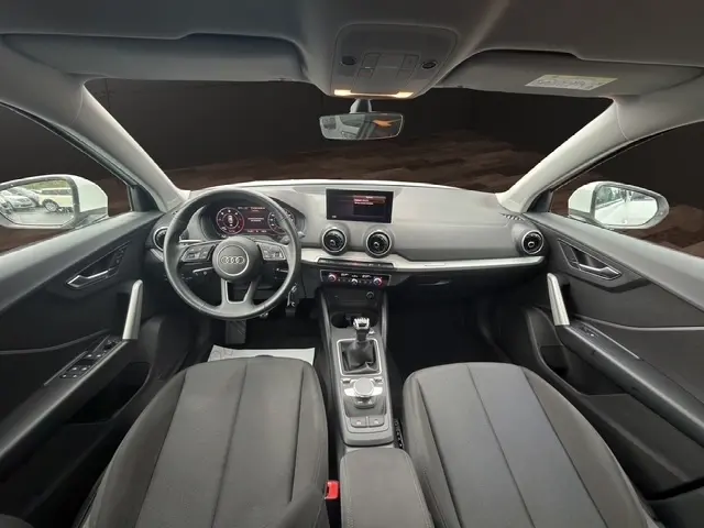 Vue intérieure avant de l'Audi Q2 blanc 30 TDI 116 Design 2021, tableau de bord moderne avec écran tactile et volant cuir multifonctions.