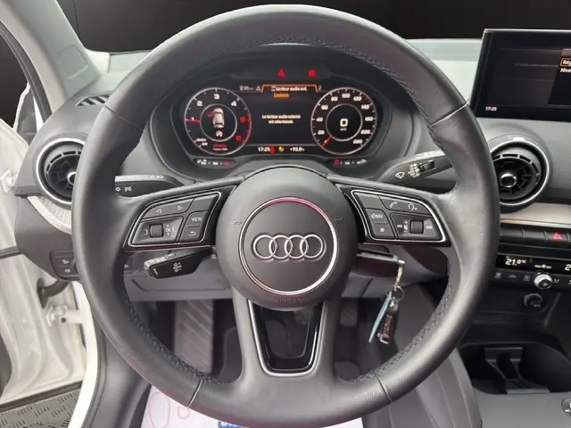 Vue centrée sur le volant cuir noir d’un Audi Q2 blanc 2021, avec tableau de bord numérique et écran tactile visible.