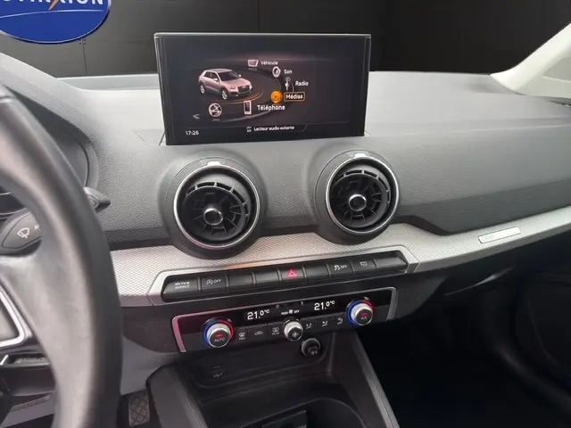 Vue intérieure du tableau de bord de l'Audi Q2 blanc 30 TDI 116 Design, avec écran tactile et aérateurs ronds centraux.