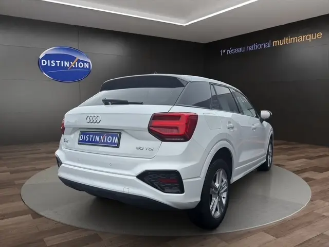 Vue de profil côté gauche d'un Audi Q2 30 TDI blanc, avec jantes alliage et toit noir dans un showroom.
