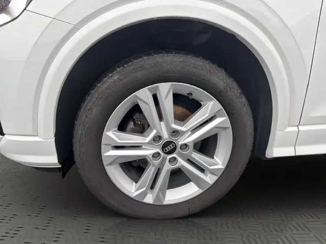 Audi Q2 30 TDI blanc vue de face, avec calandre noire hexagonale et phares LED allumés dans un showroom.