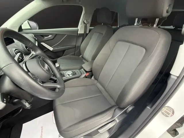 Vue intérieure côté conducteur de l'Audi Q2 blanc 30 TDI 116 Design, sièges tissu gris et volant cuir multifonctions.