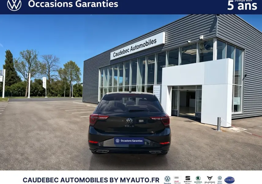 Vue arrière d'une Volkswagen Polo noire intense nacrée stationnée devant un bâtiment moderne de concession.