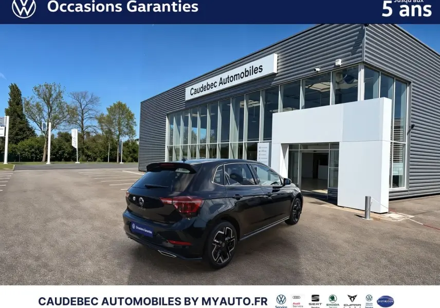 Vue 3/4 arrière droite d'une Volkswagen Polo noire intense nacrée stationnée devant un bâtiment moderne de concession.