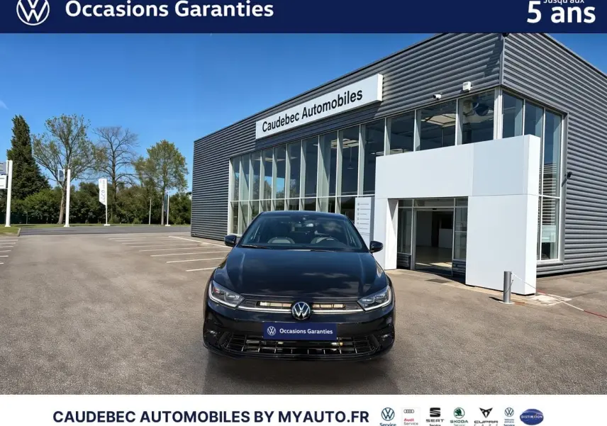 Vue frontale d'une Volkswagen Polo noire intense nacrée garée devant un bâtiment moderne de concession automobile.