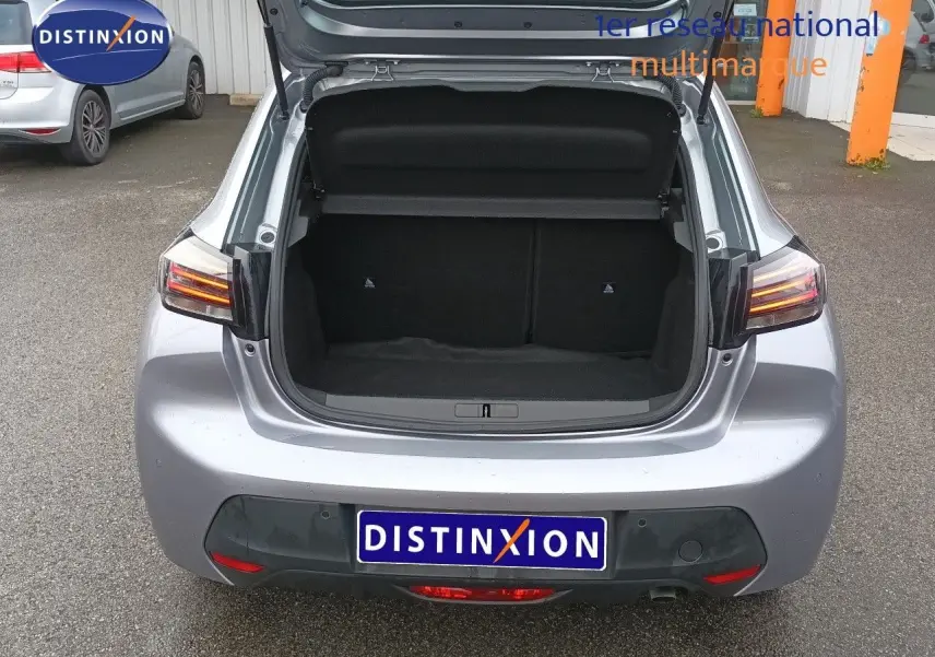 Vue arrière ouverte sur le coffre d'une Peugeot 208 gris Artense métal, avec feux arrière allumés et plaque Distinxion.
