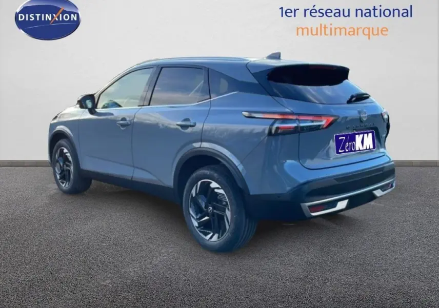 Vue 3/4 arrière droite d'un Nissan Qashqai gris 2025 avec jantes aluminium et barres de toit visibles.